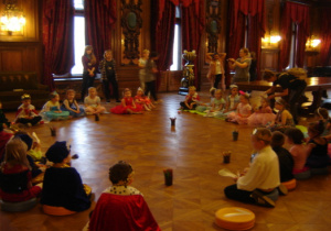 Dzieci siedzą w balowych strojach w Sali Balowej w Pałacu I. Poznańskiego.